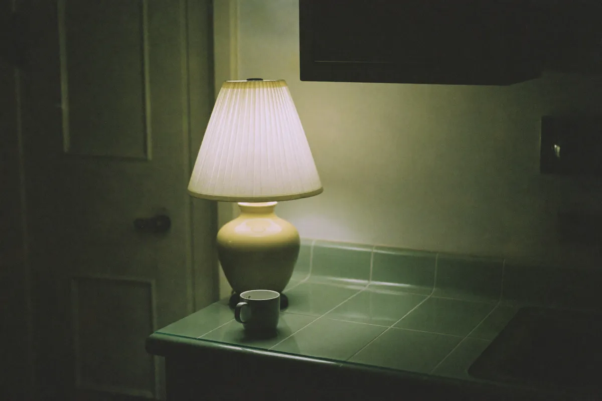 A single lamp and a forgotten mug in a quiet kitchen at night, the rest of the house asleep