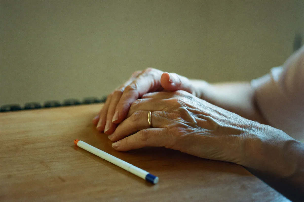 The hands of a woman in her forties resting on a kitchen table beside a pen, part way through working out her expression number