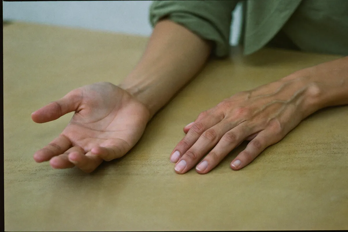 A woman's two hands resting on a table, one open and receiving, one lying flat and composed, the two energies side by side