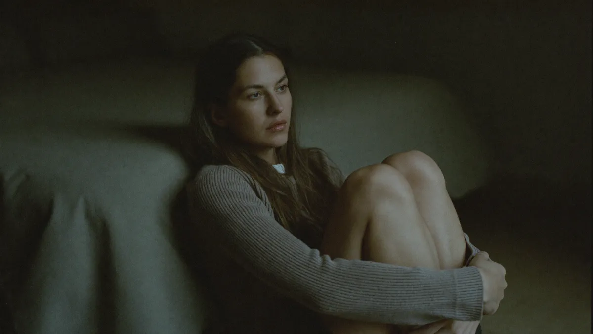 A woman sitting very still by a window, checked out and far away, the freeze response