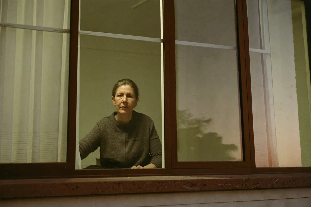 A woman in her forties seen through her kitchen window from outside, framed and composed, the outward impression a personality number describes