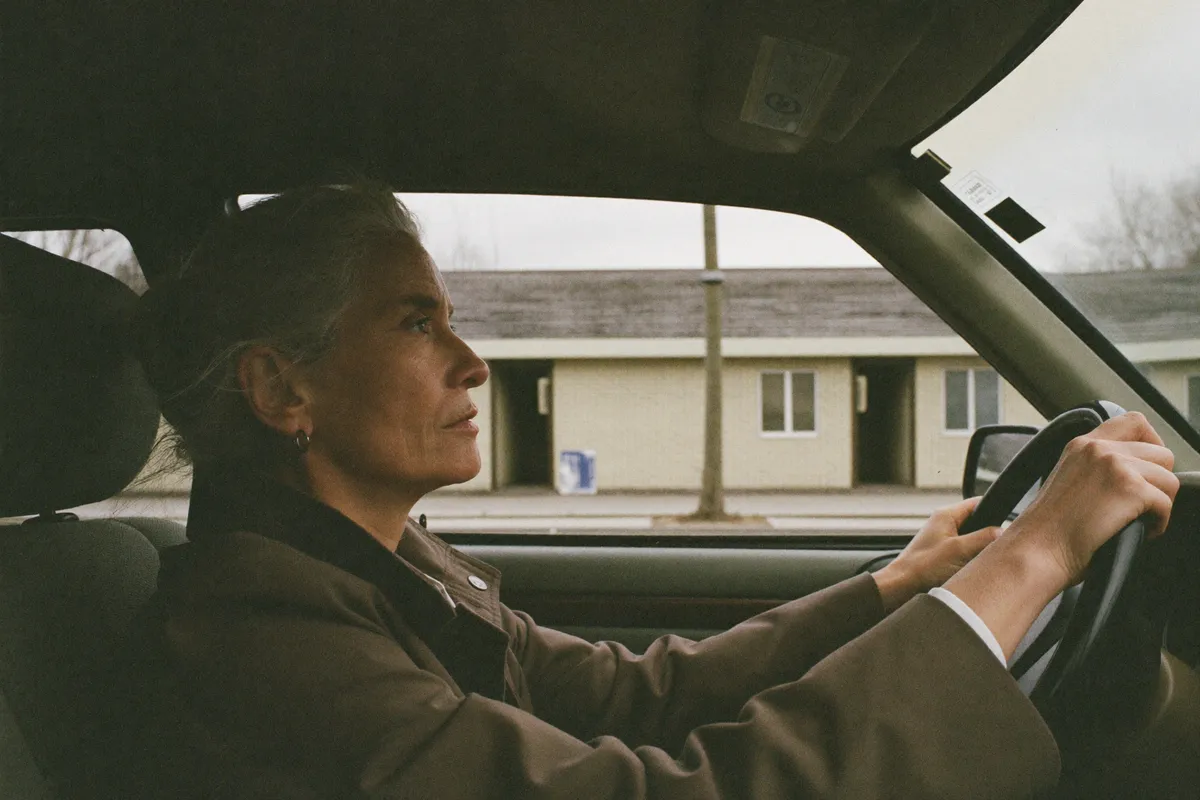 A woman sits in her parked car outside her mother's flat before driving home, the pause in the middle of a sandwich generation day