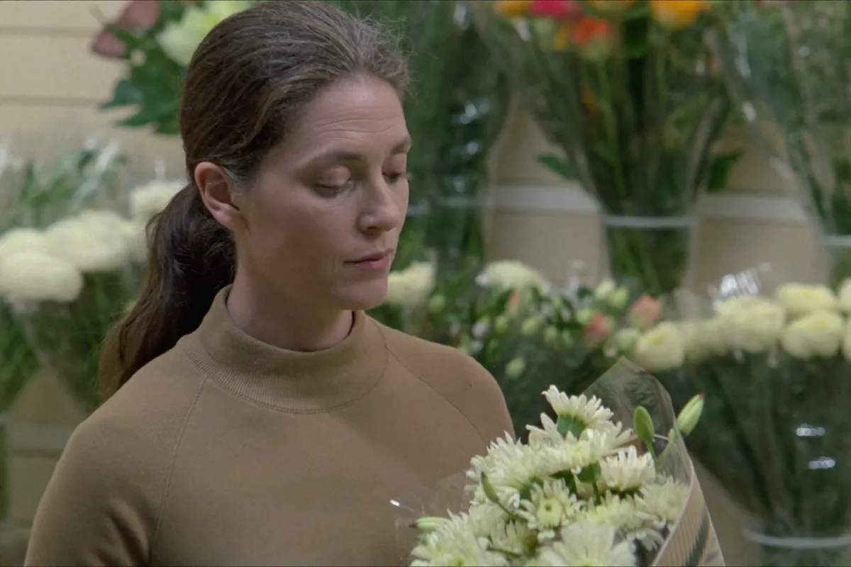 A woman in her forties in a flower aisle, looking down at a bunch of flowers she has decided not to buy