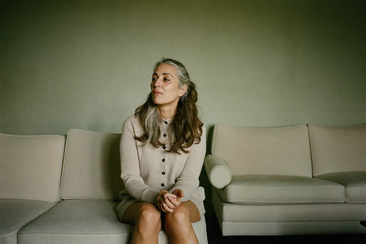 A woman in her forties sits alone on the end of a sofa in morning light, considering what she actually wants
