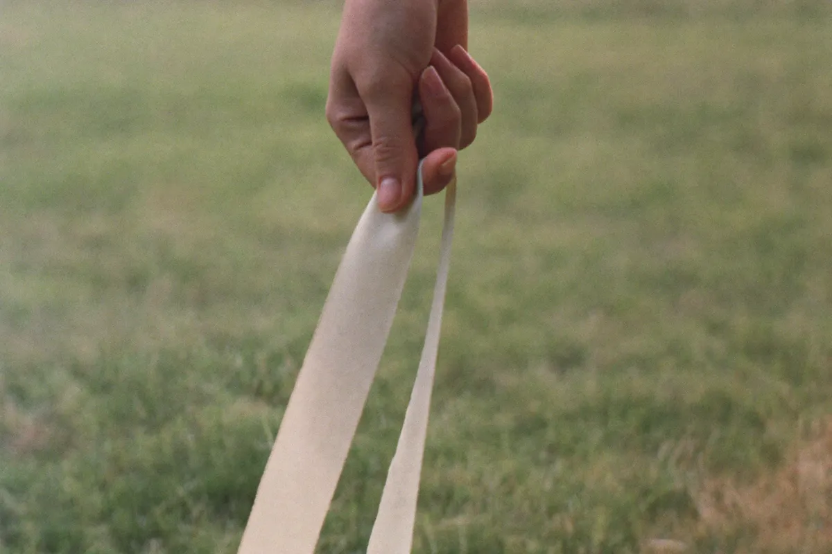 A hand loosening its grip on a ribbon and letting it slip free, the small act of allowing that loosens control